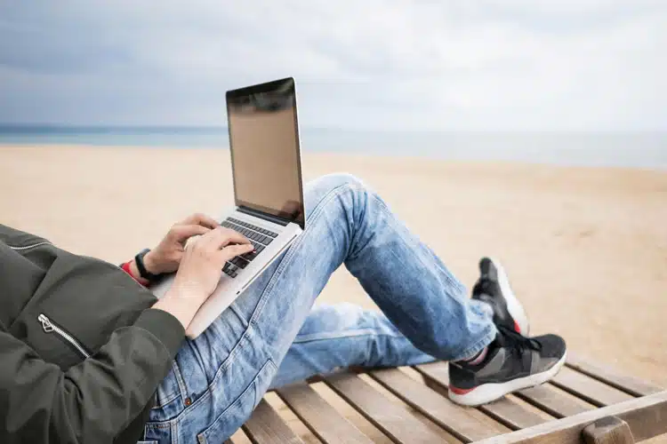 Image of someone sat on the beach on their laptop.