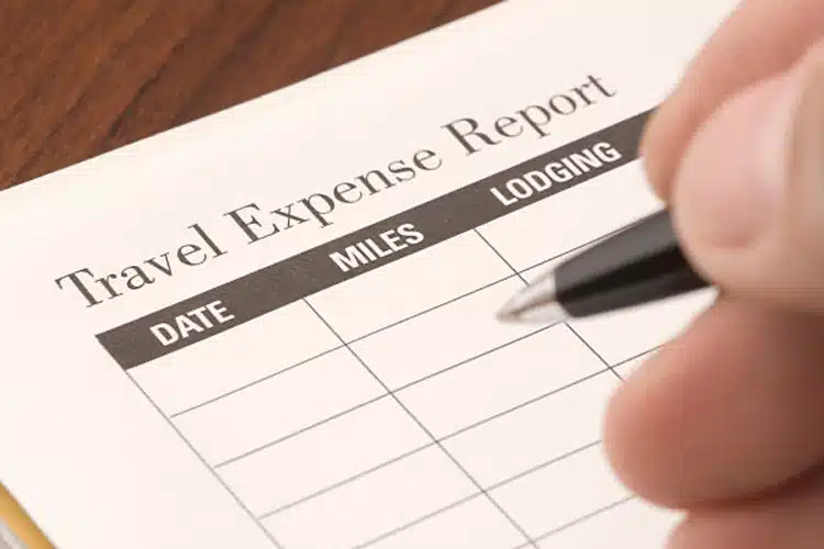 Paper with the title travel expense report and a hand holding a pen